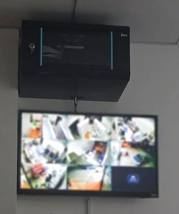 Wall-mounted network cabinet above a CCTV monitor in a shop (screen blurred)